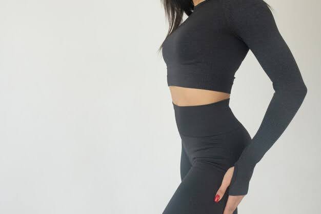 A woman in a fitted black long-sleeve crop top and high-waisted leggings poses stylishly.